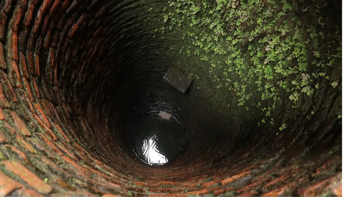 Deep view down an old brick-lined well shaft with water at the bottom