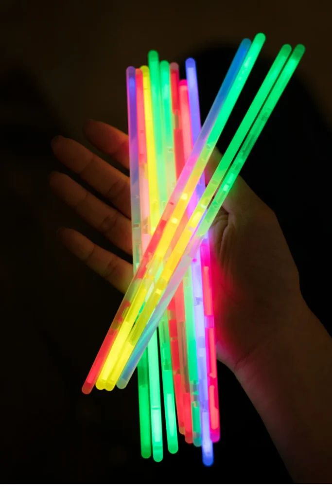 A hand holding a bundle of colorful glowing glow sticks in the dark