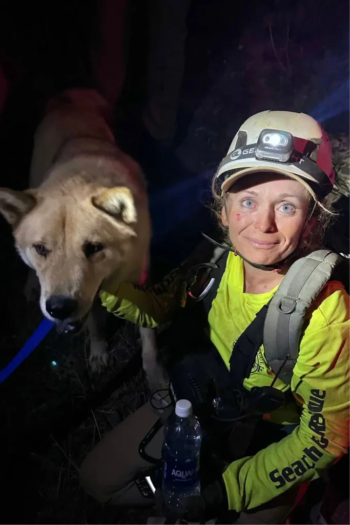 Search and rescue volunteer in a helmet with headlamp kneeling beside the rescued dog at night