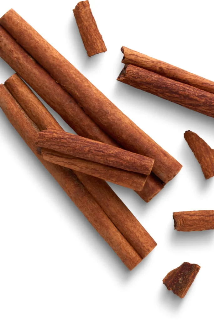 Whole and broken cinnamon sticks scattered on a white background